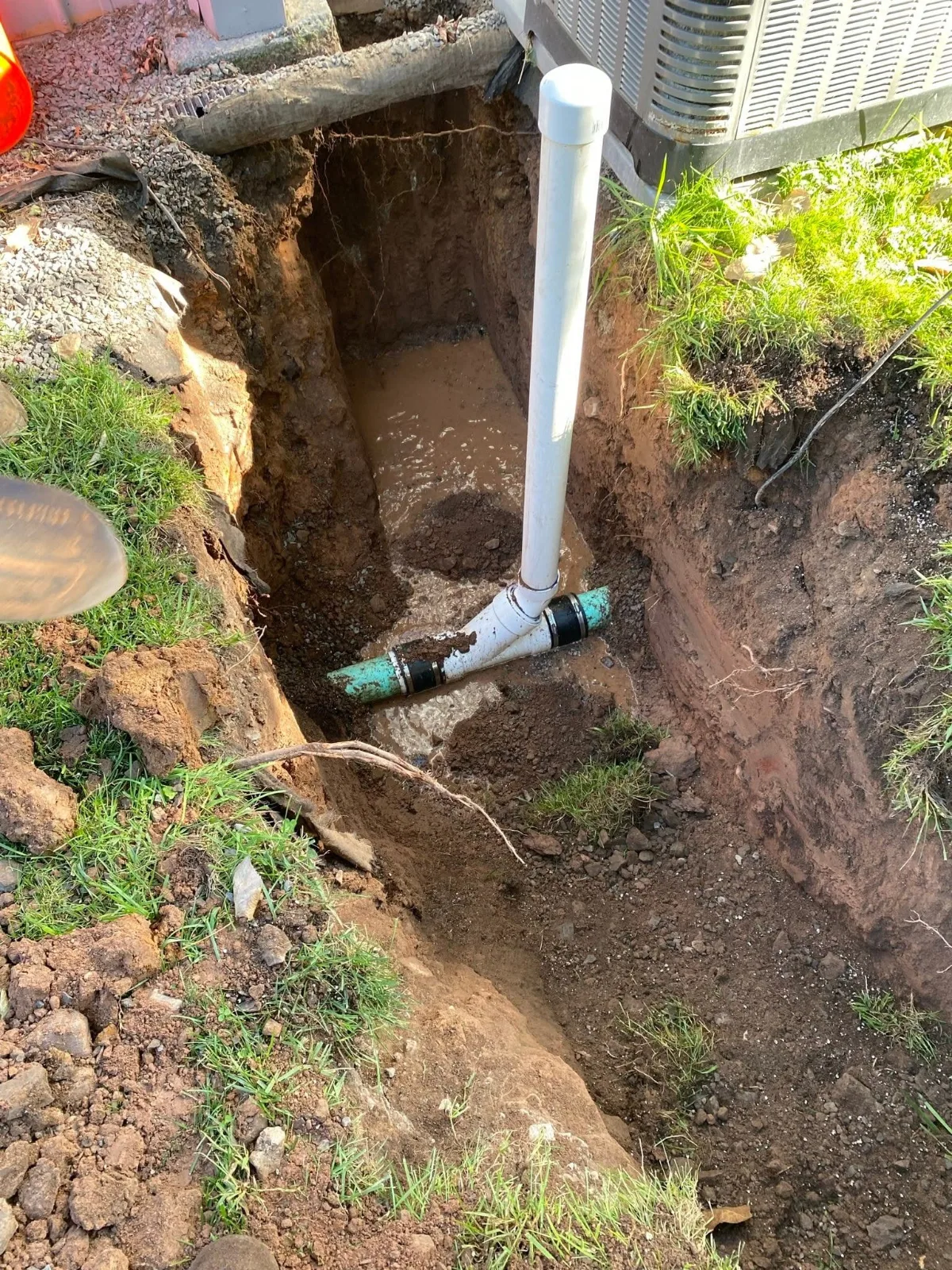 A sewer pipe repair in an open hole beside a house, with a new cleanout riser