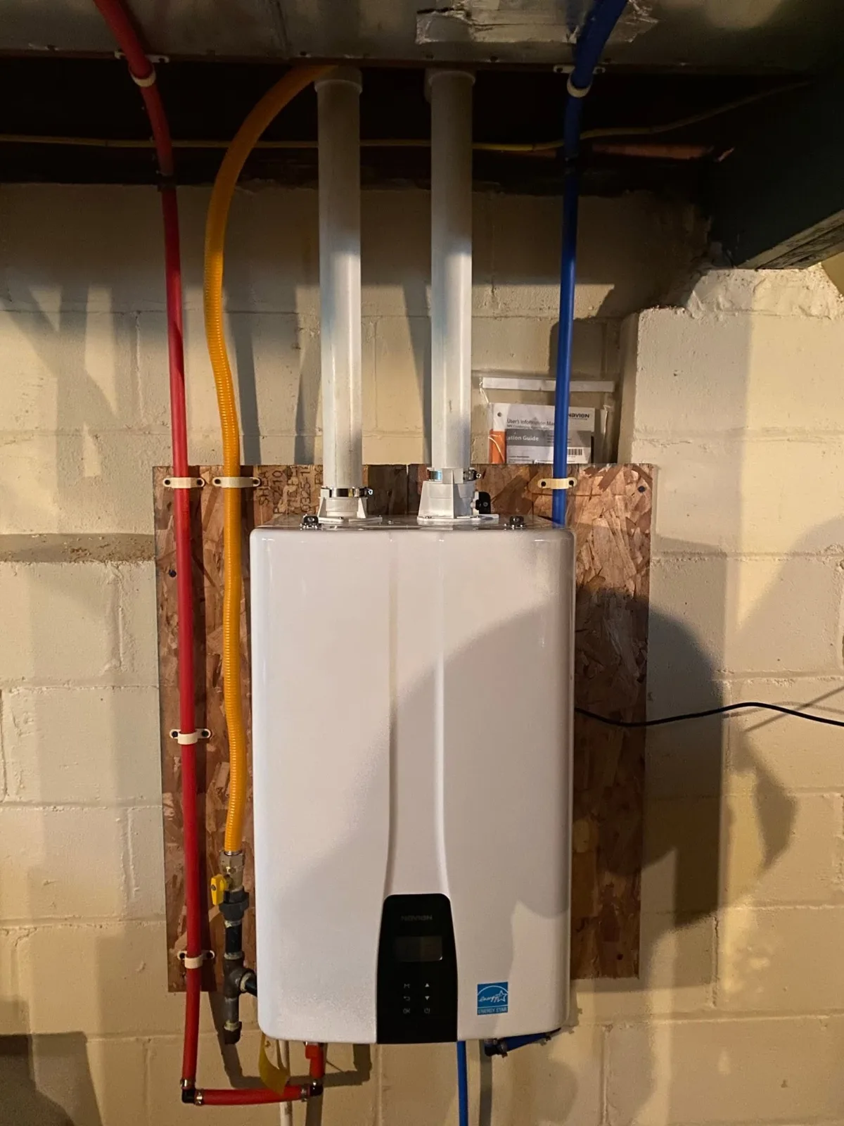 A Navien tankless water heater on a basement wall, its venting, gas and water lines run
